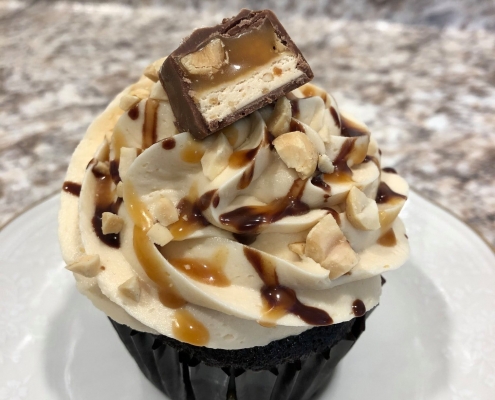 Snitger Sweet Cupcake: Chocolate cupcake with caramel buttercream, chocolate ganache and caramel sauce drizzle, chopped peanuts and a Snickers candy bar slice